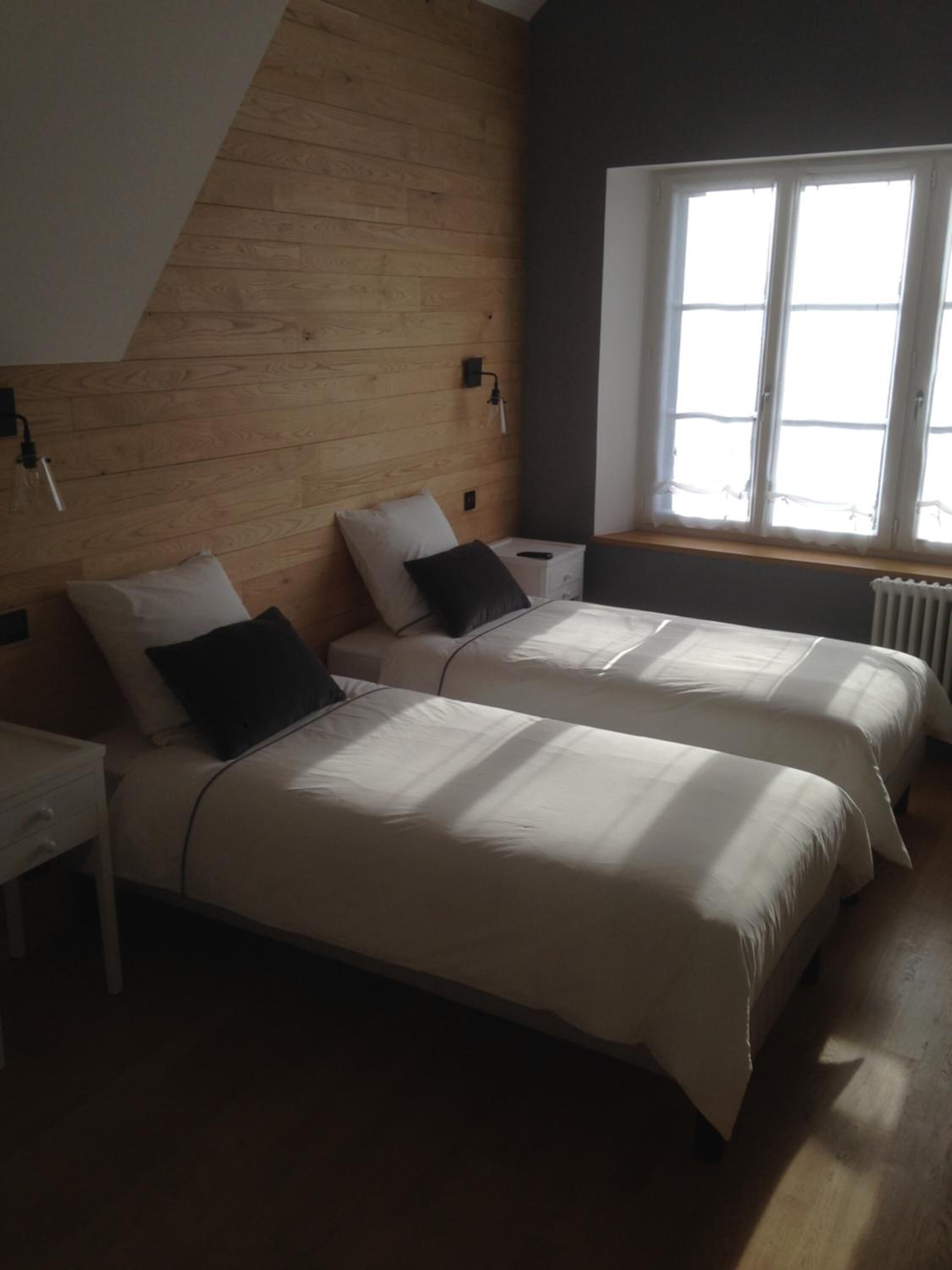 Une chambre avec deux lits, des murs en bois, une fenêtre et un radiateur.