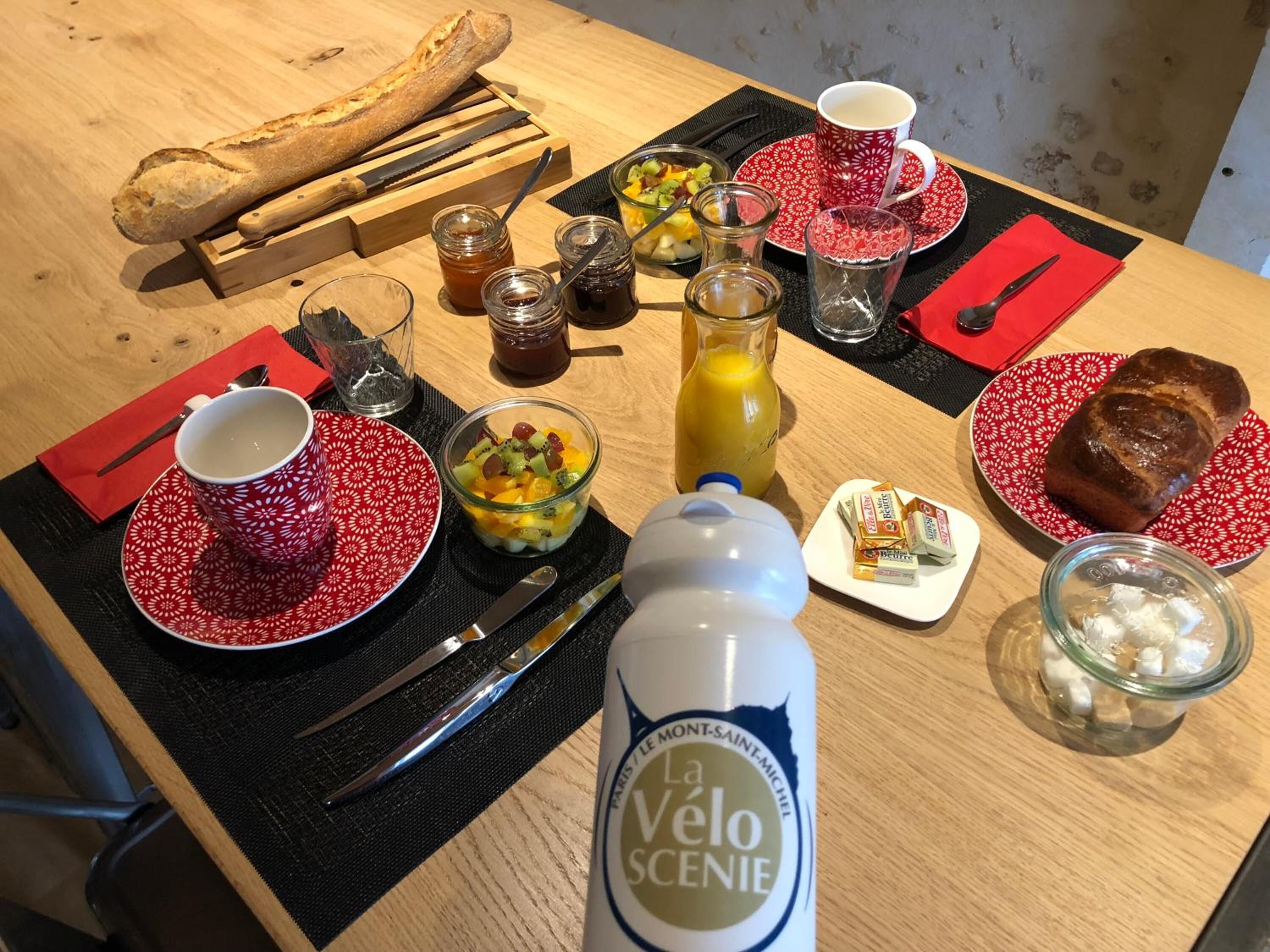 A breakfast setting with bread, fruit, jam, and a bottle of La Velo Scenie.