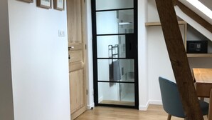 Un intérieur moderne avec un plancher en bois, un escalier et une porte en verre donnant sur un espace cuisine.