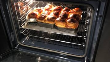Um forno com visor digital mostrando a hora 13:21. No interior, duas assadeiras com produtos de panificação, possivelmente pão ou doces, no nível do meio.
