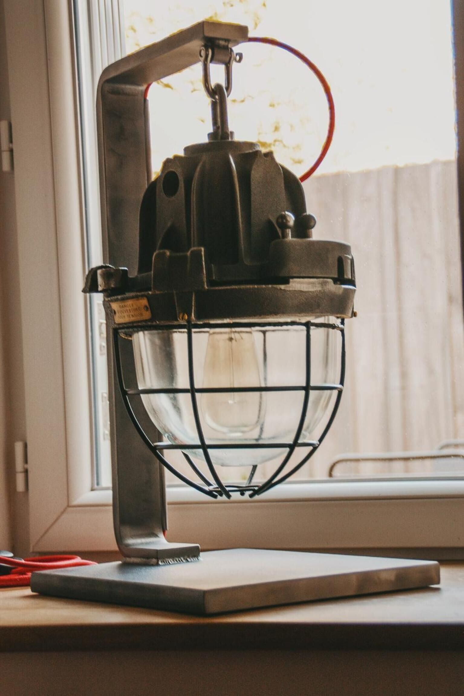 Uma luminária de mesa estilo vintage com base de metal e cobertura de vidro, apoiada num peitoril de janela.