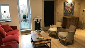 Un salon avec un canapé rouge, une table basse en bois, deux fauteuils et un tableau décoratif au mur.