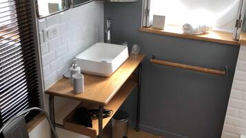 Un baño pequeño con lavamanos blanco, un espejo, toallero y una ventana.