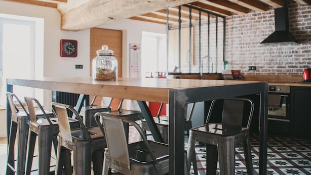 Une cuisine avec des poutres apparentes, un mur en briques et un grand îlot central doté de chaises.