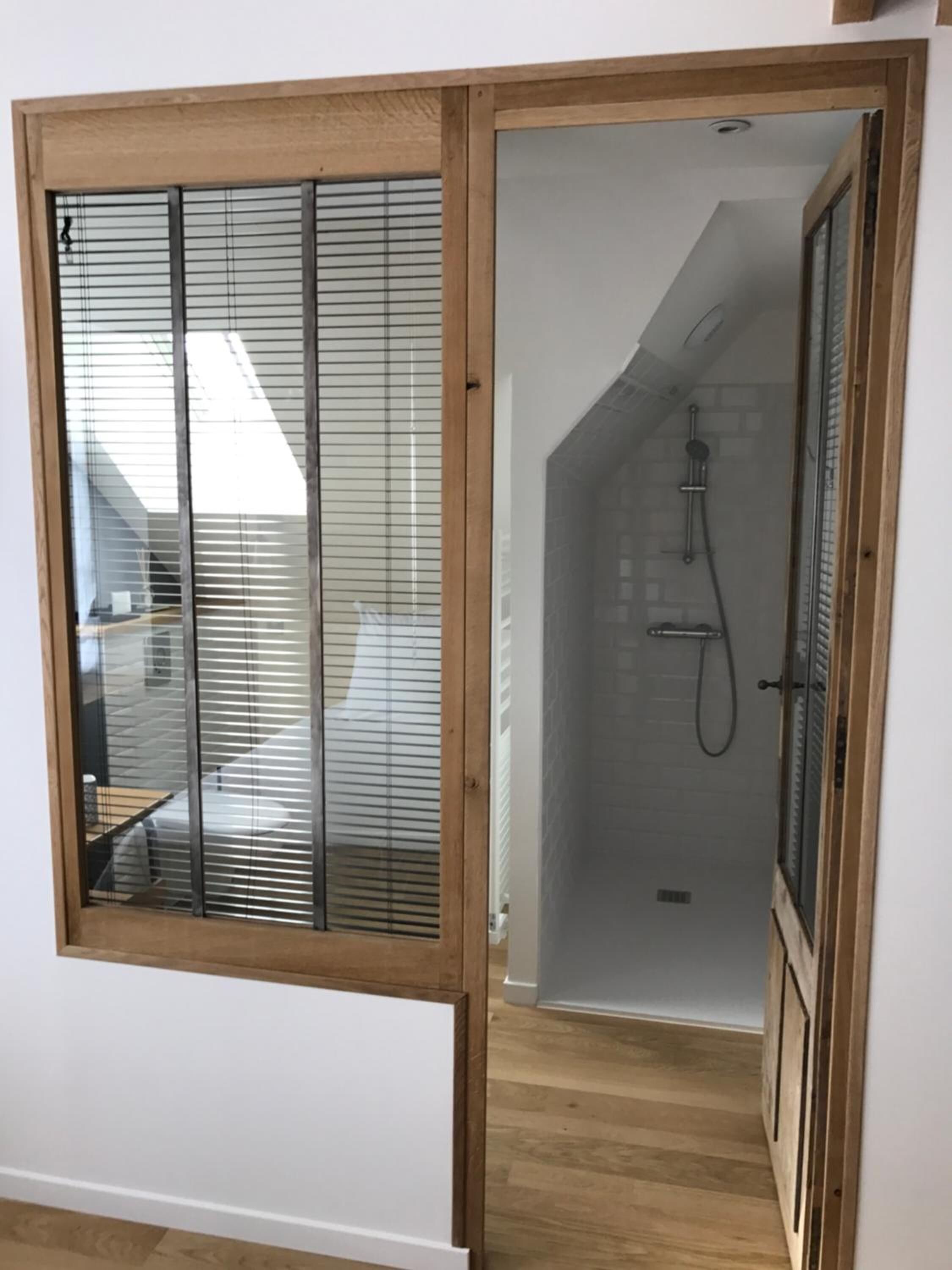 A room with a sliding glass door leading to a shower area with a tiled wall and a wooden floor.