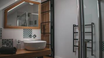 Un baño moderno con un espejo grande, un tocador de madera, un lavabo blanco y una cabina de ducha de vidrio.