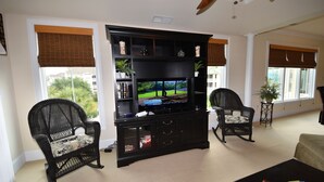 A living room with a flat-screen TV, two wicker chairs, a coffee table, and a bookshelf. - Edgewater Apartment 437 (North Myrtle Beach)