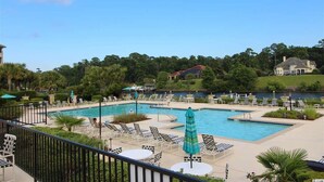 A pool area with lounge chairs and umbrellas, surrounded by greenery and a body of water. - Edgewater Apartment 437 (North Myrtle Beach)