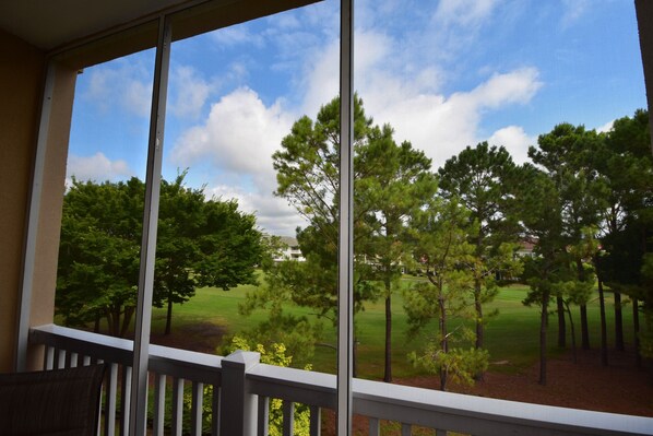 A view from a balcony with a railing, overlooking a grassy area with trees and a building in the distance.