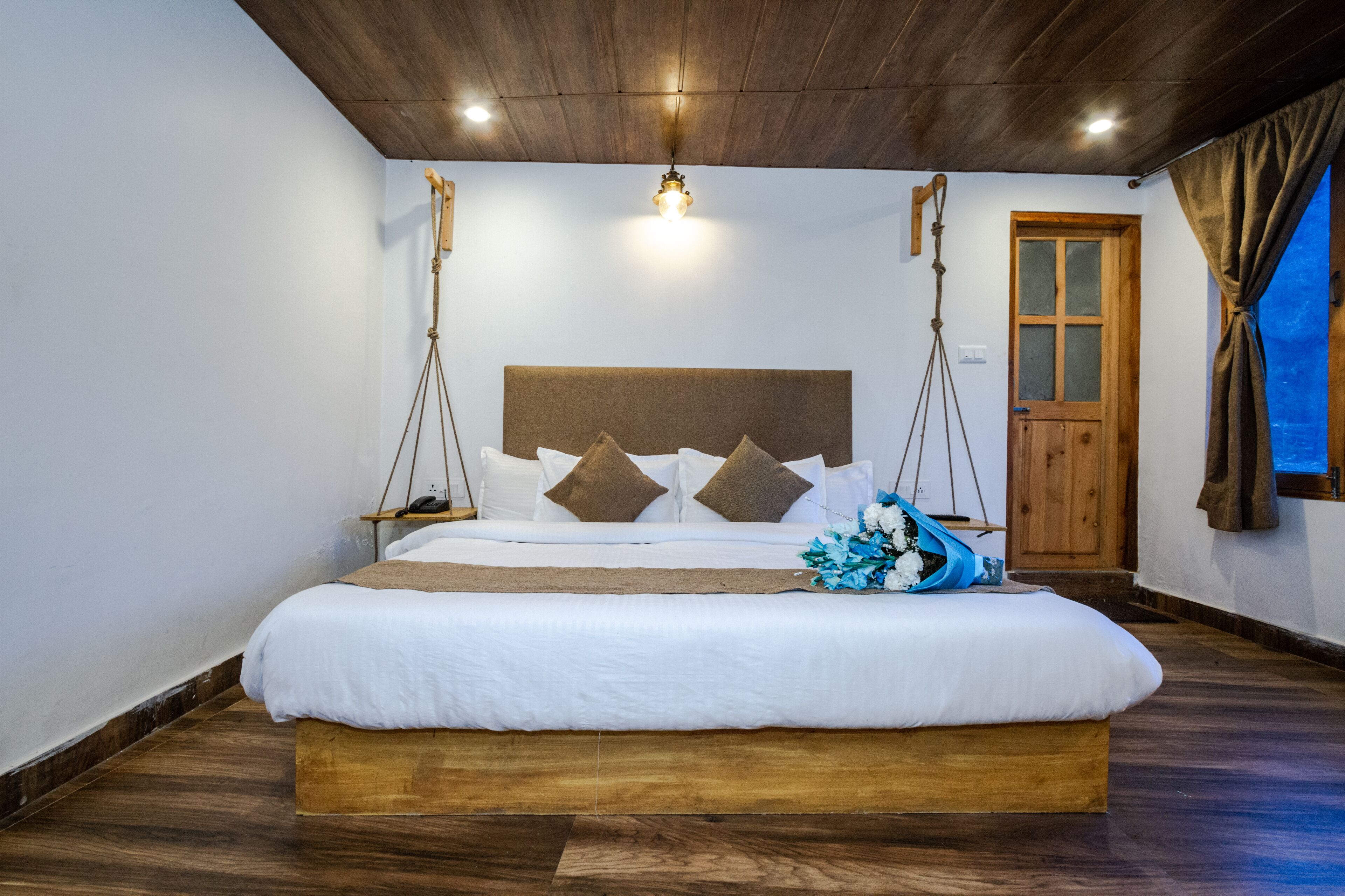 A large bed with a wooden headboard, white bedding, and a decorative blue flower arrangement.