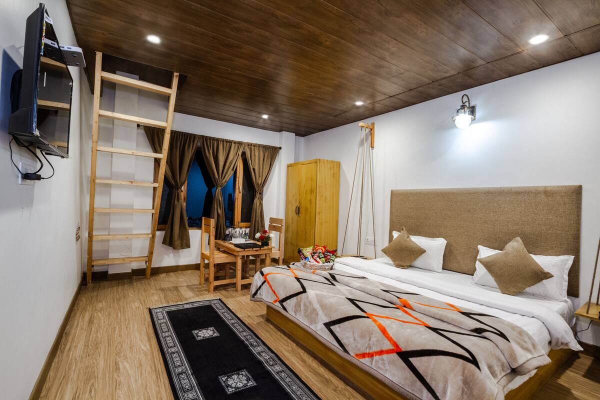 Un dormitorio con techo de madera, una cama con colcha estampada, un escritorio con silla, un armario y un televisor fijado a la pared.