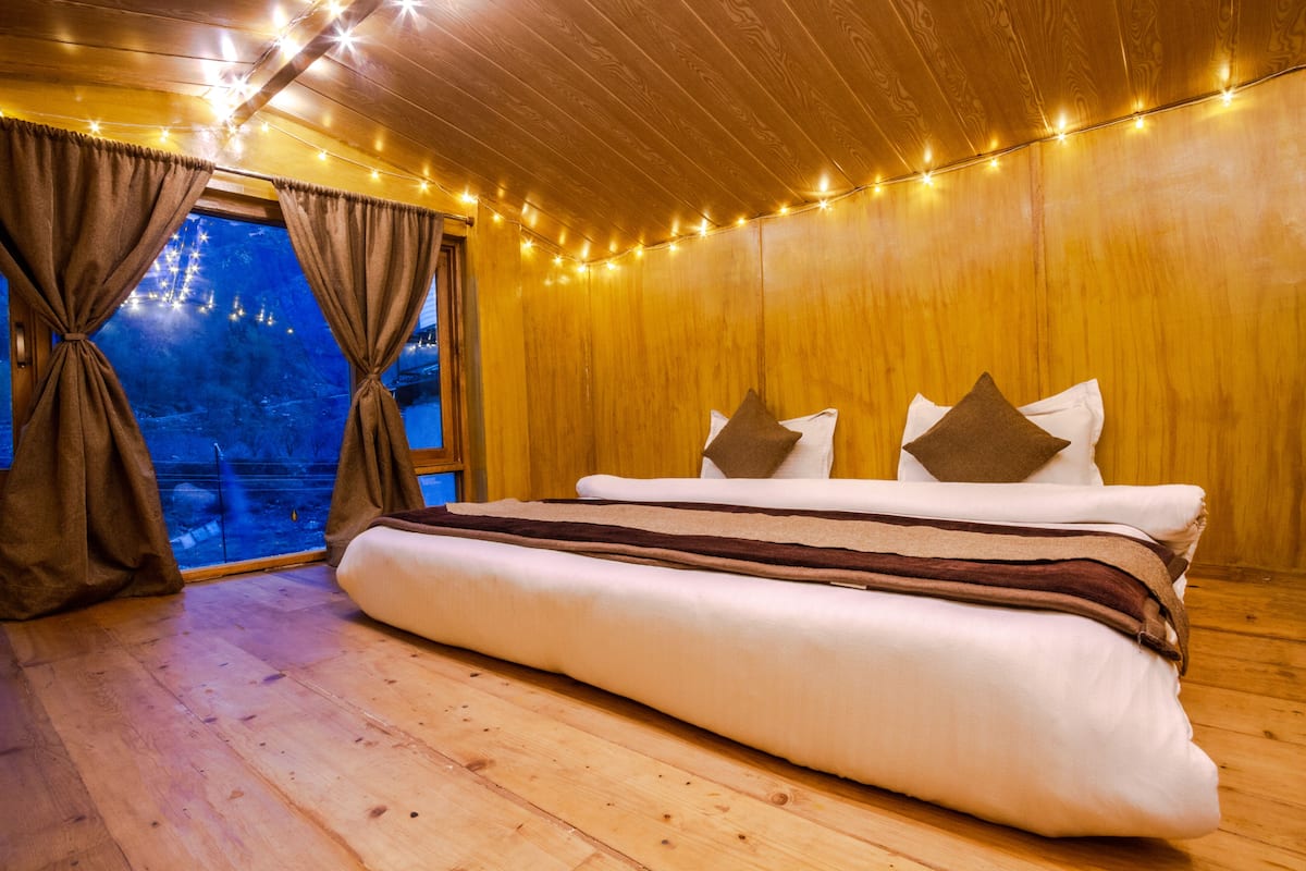 Una habitación acogedora con suelo de madera, una cama con almohadas y luces colgantes.