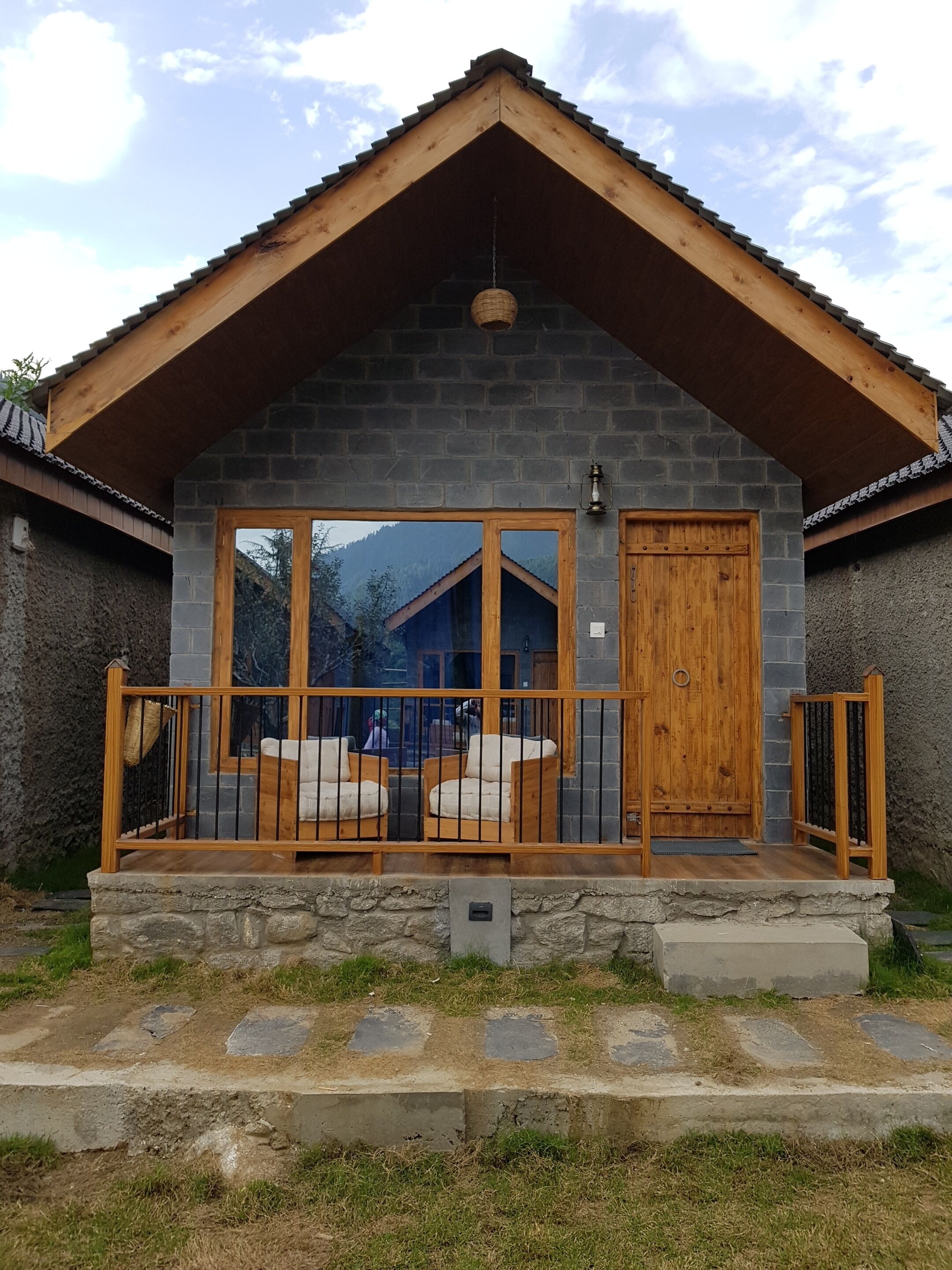A rustic cabin with a stone facade, large glass windows, and a wooden deck with outdoor seating.