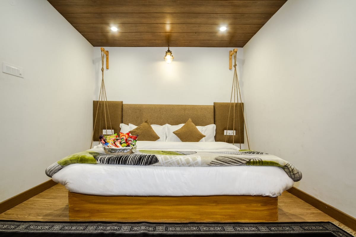 Una cama bien hecha con cabecera de madera, una mesita de noche con un recipiente de bocadillos y una lámpara colgante encima.