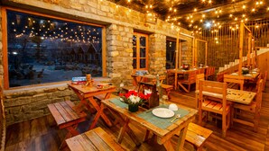 Un interior rústico de madera con paredes de piedra, mesas y bancos de madera, y luces colgantes.