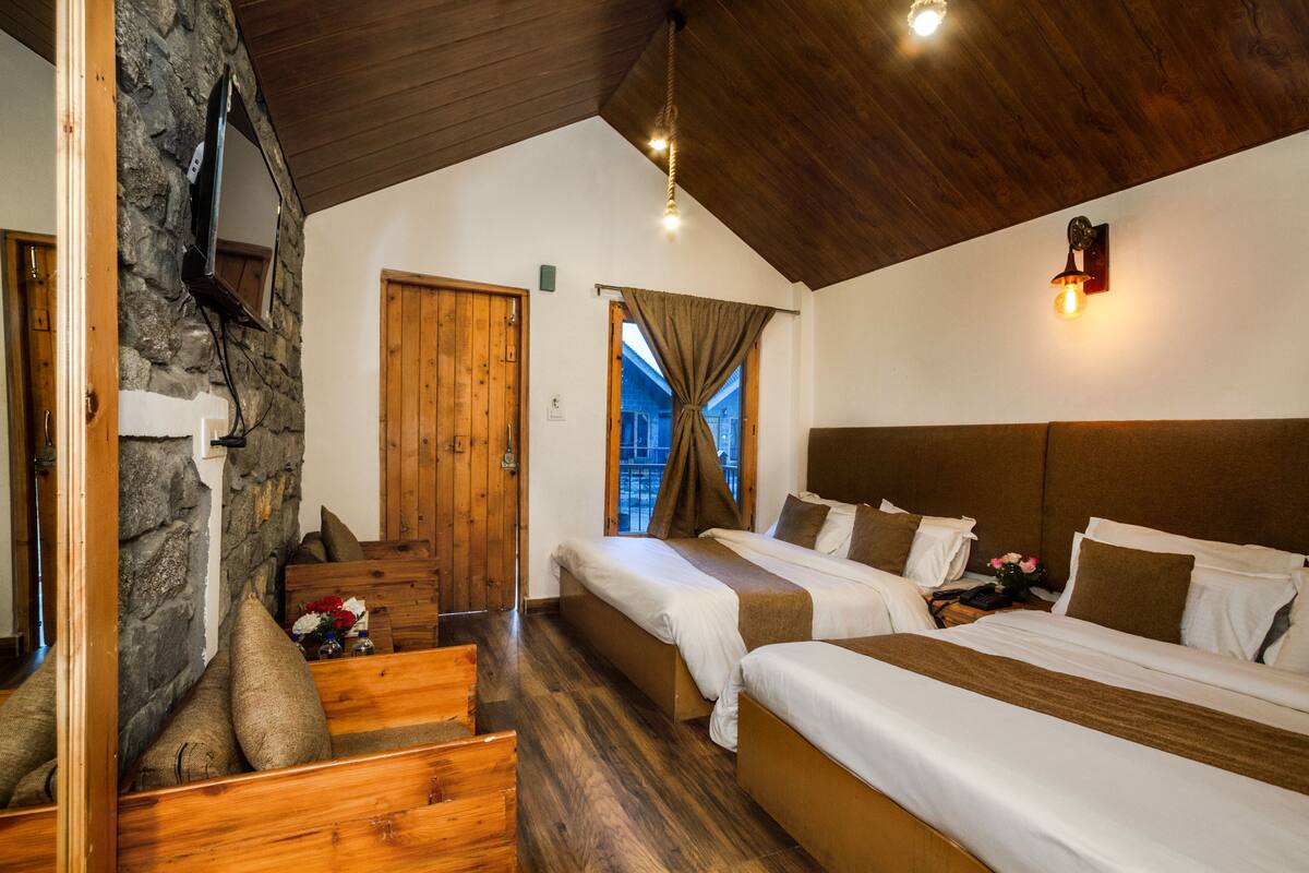 Una habitación con dos camas, suelo de madera, pared de piedra y techo de madera.