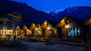 Un albergue con varias cabañas de madera, mobiliario exterior y vistas a montañas nevadas.