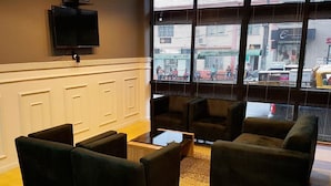 A modern lobby with dark sofas, a coffee table, and a TV mounted on the wall.