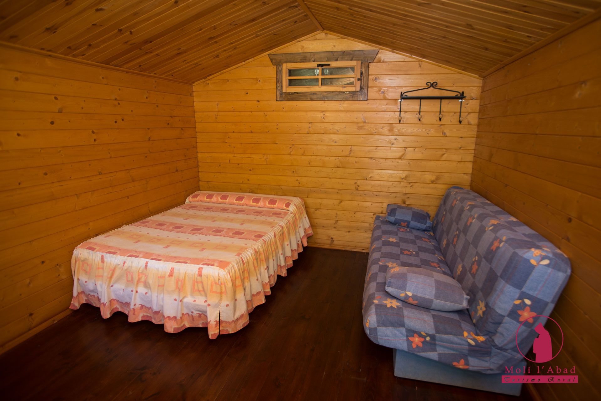 Una pequeña habitación tipo cabaña de madera, con cama y sofá.