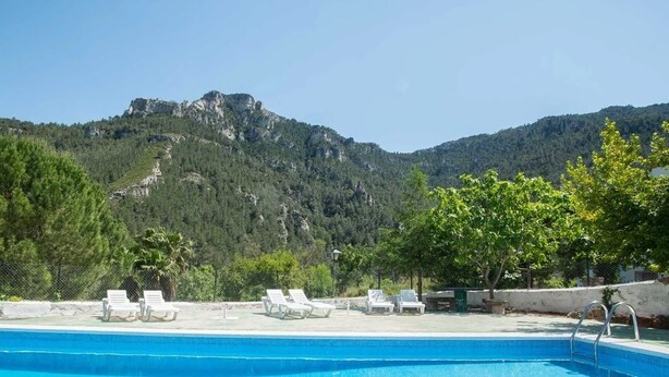 Ein Schwimmbecken mit Liegestühlen und einer Bergkulisse im Hintergrund.