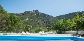 Una piscina con sillones de descanso y montañas al fondo.