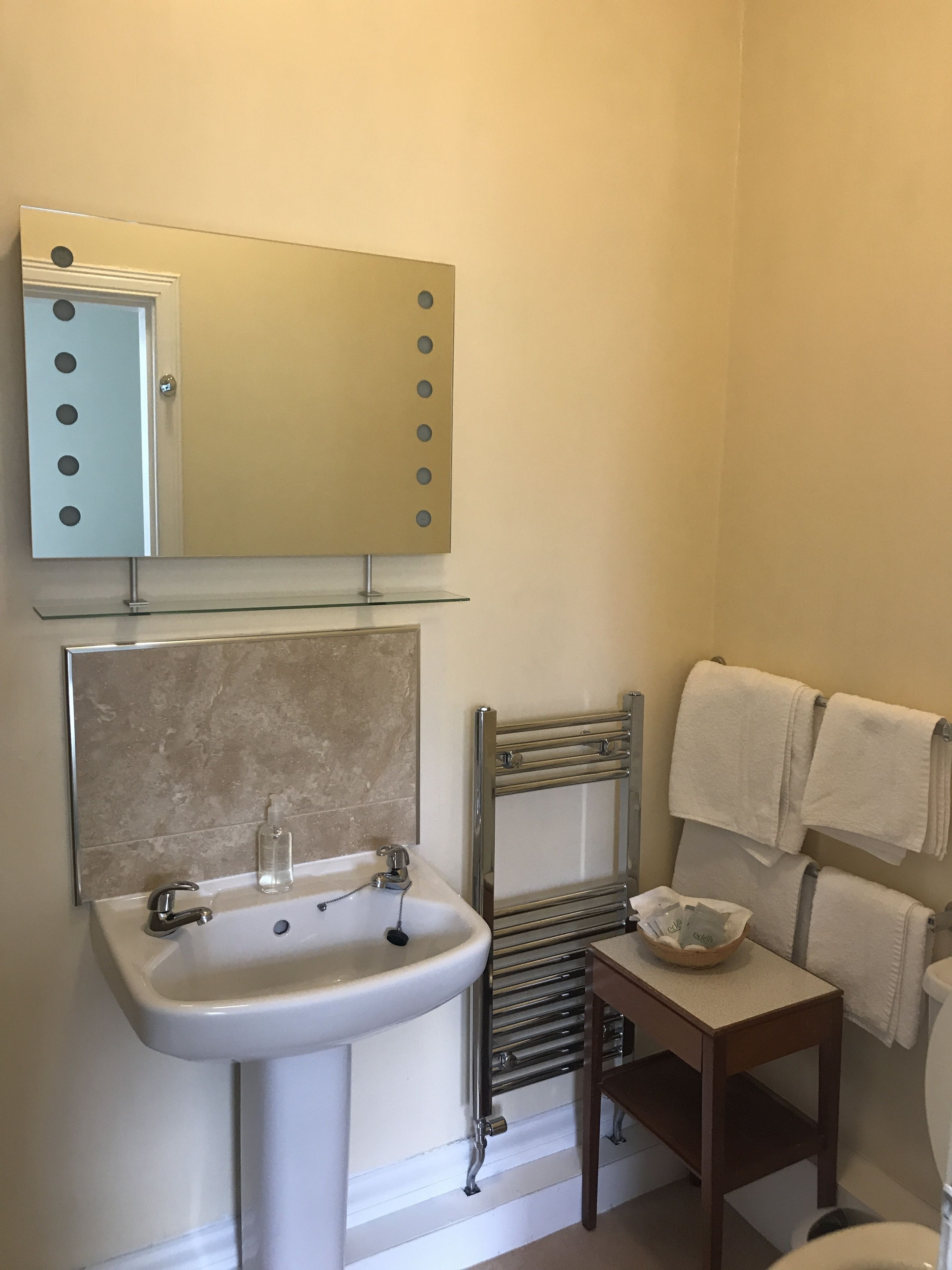 A bathroom with a sink, mirror, towel rack, and a small table with a bowl.
