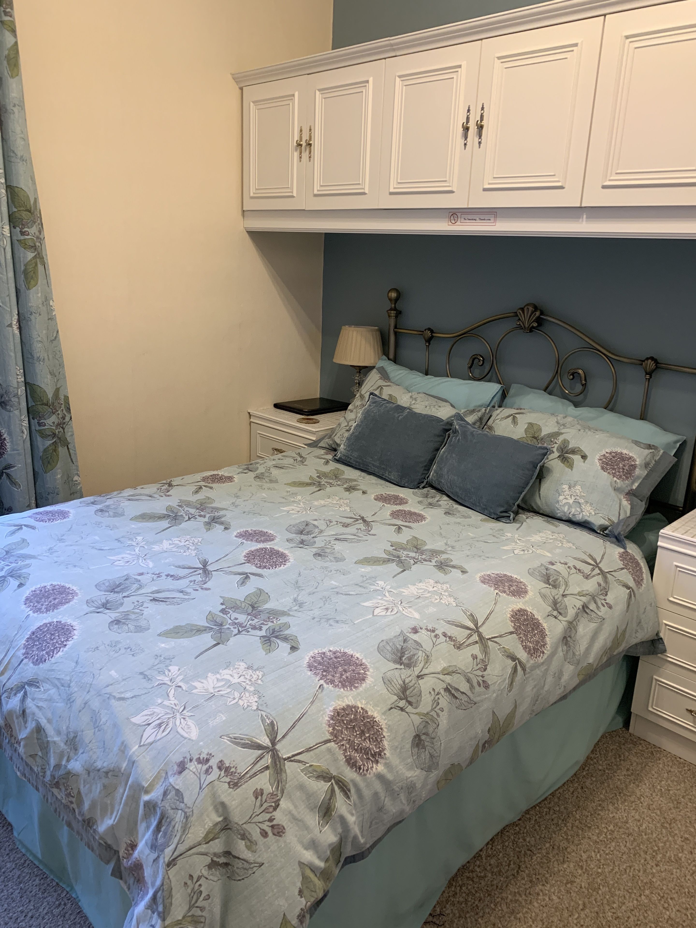 A bedroom with a floral bedspread, a metal headboard, white nightstands, and a white wardrobe.