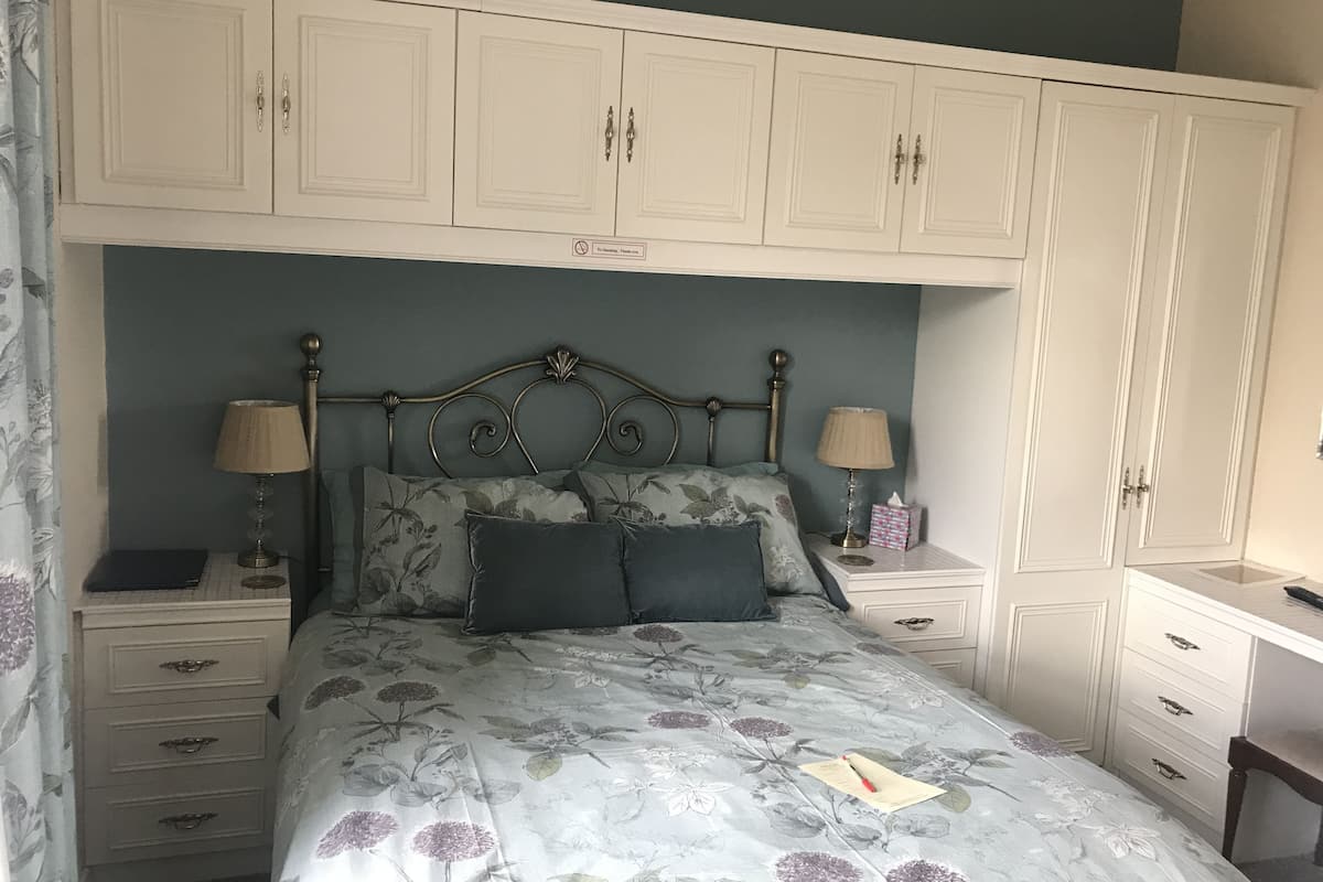 A bedroom with a bed, two bedside tables, a desk, and a wardrobe.