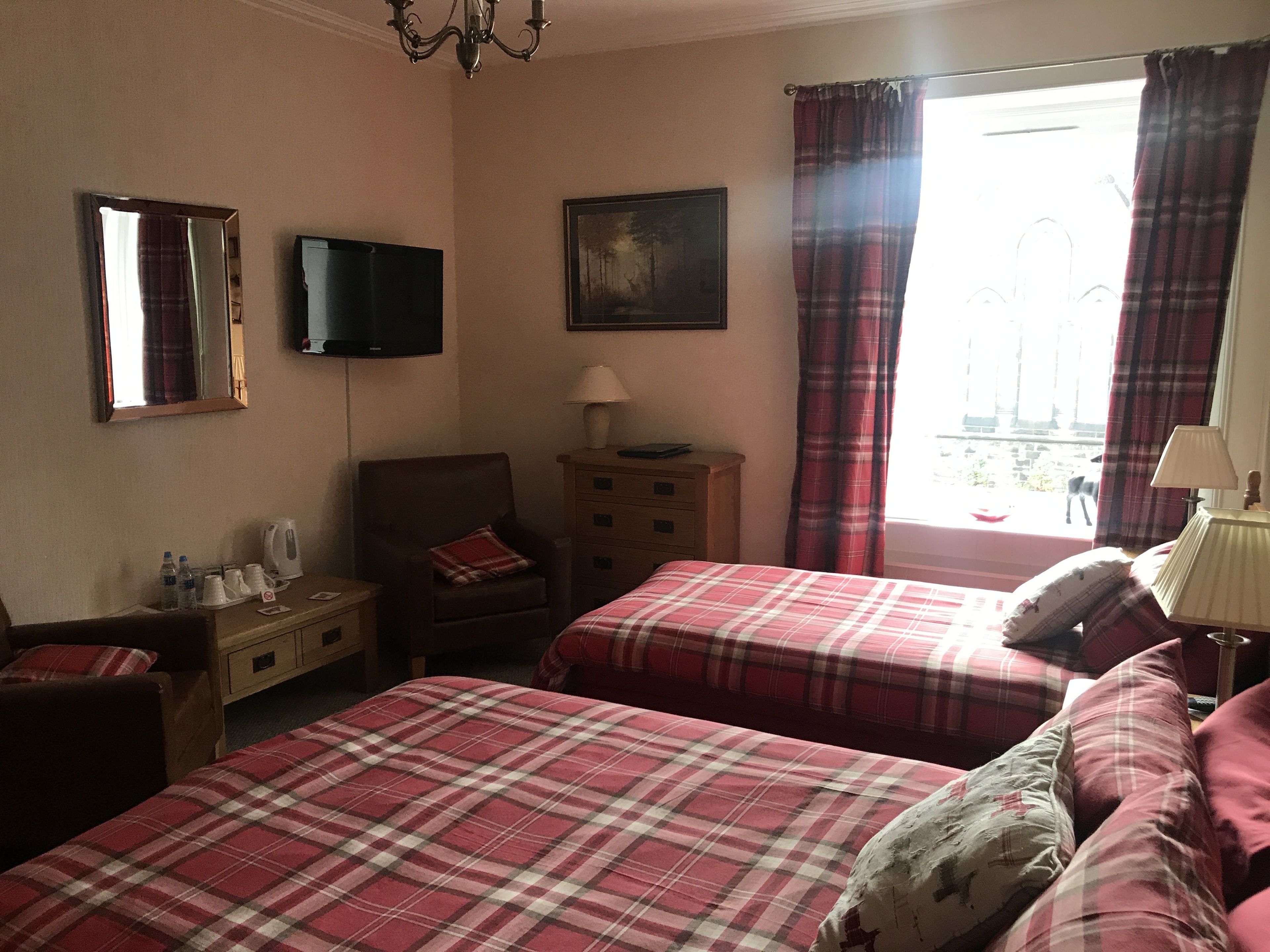 A hotel room with two beds, a TV, a painting, a chair, a nightstand, and a window with curtains.