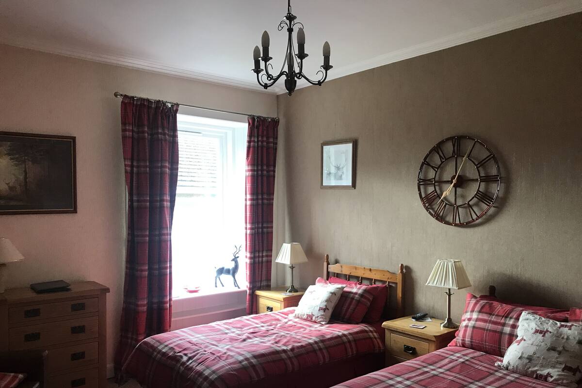 A bedroom with two beds, a wooden dresser, a nightstand, a wall clock, and a chandelier.