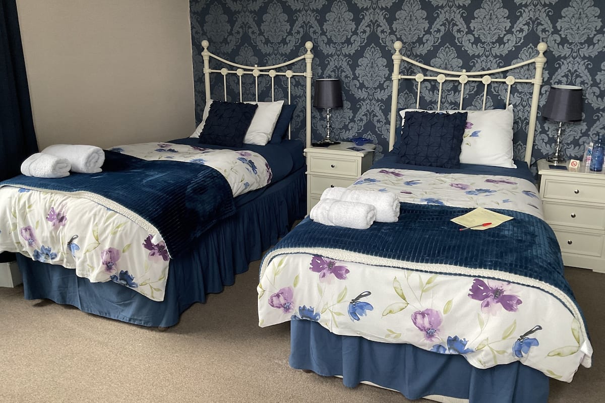 Two twin beds with floral bedding, a nightstand with a lamp, and a wall with a patterned wallpaper.
