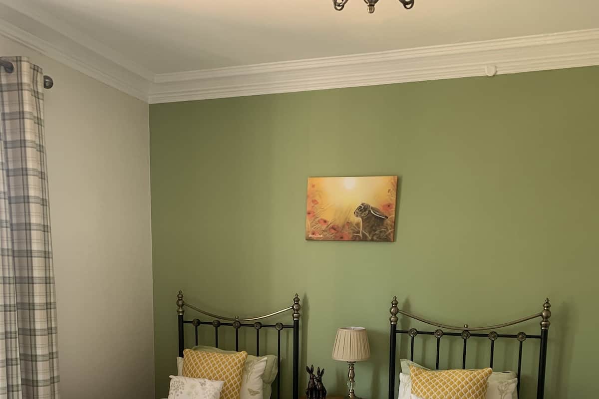 A bedroom with two single beds, a nightstand with a lamp, and a painting on the wall.