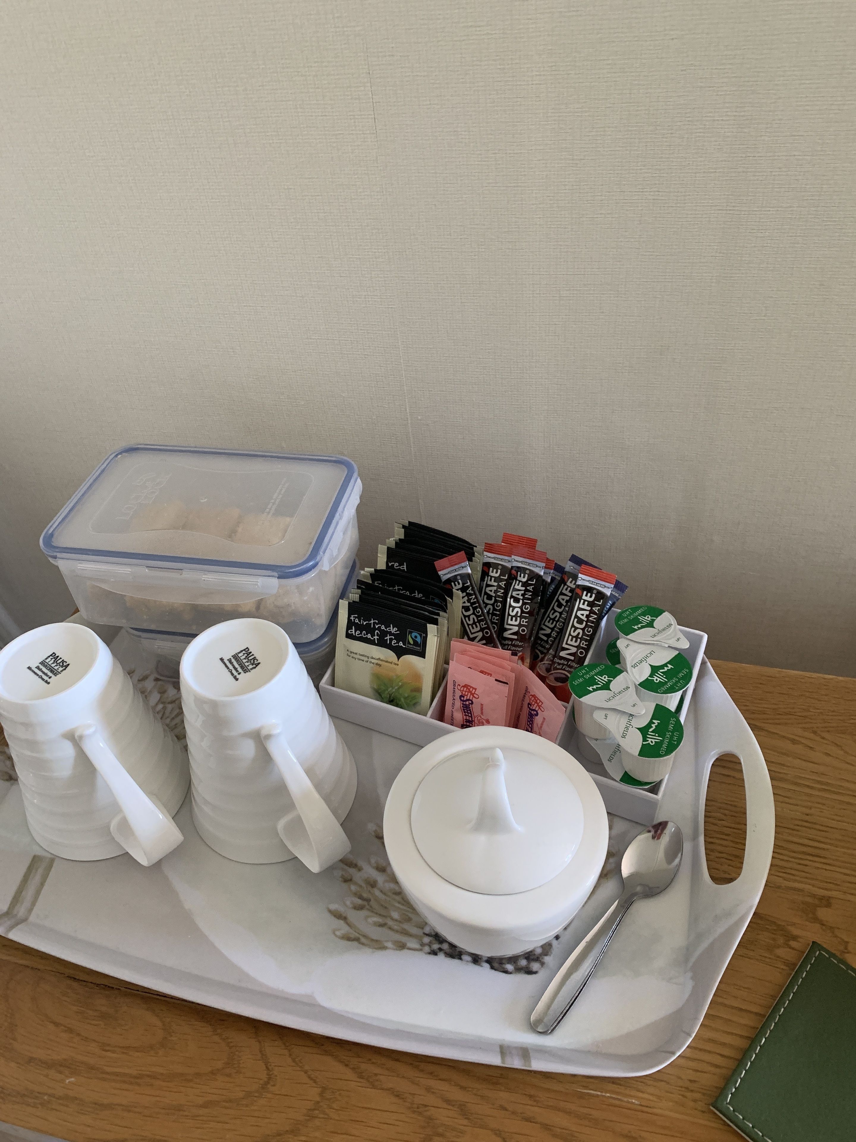 A tray with two white mugs, a container of sugar, a box of Nescafé Original coffee pods, and a spoon.