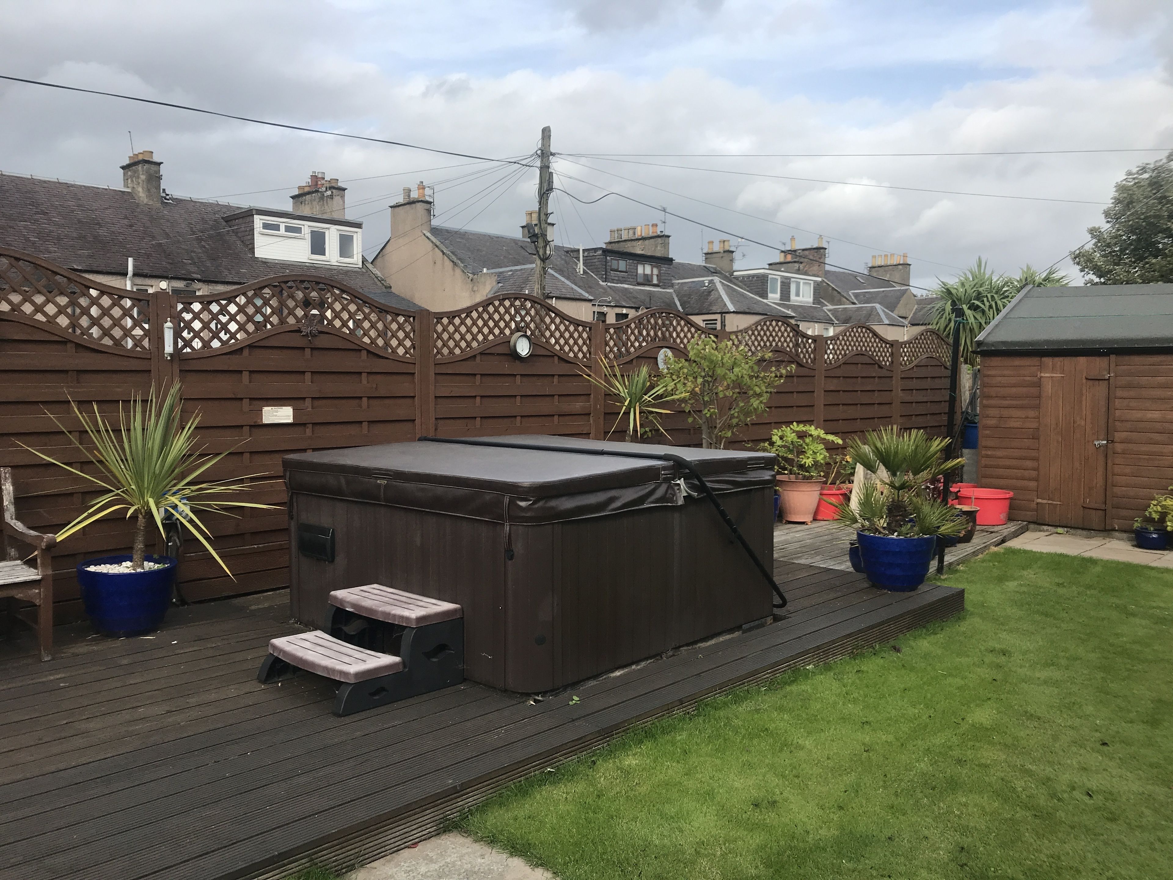 A backyard with a hot tub, wooden deck, and potted plants.