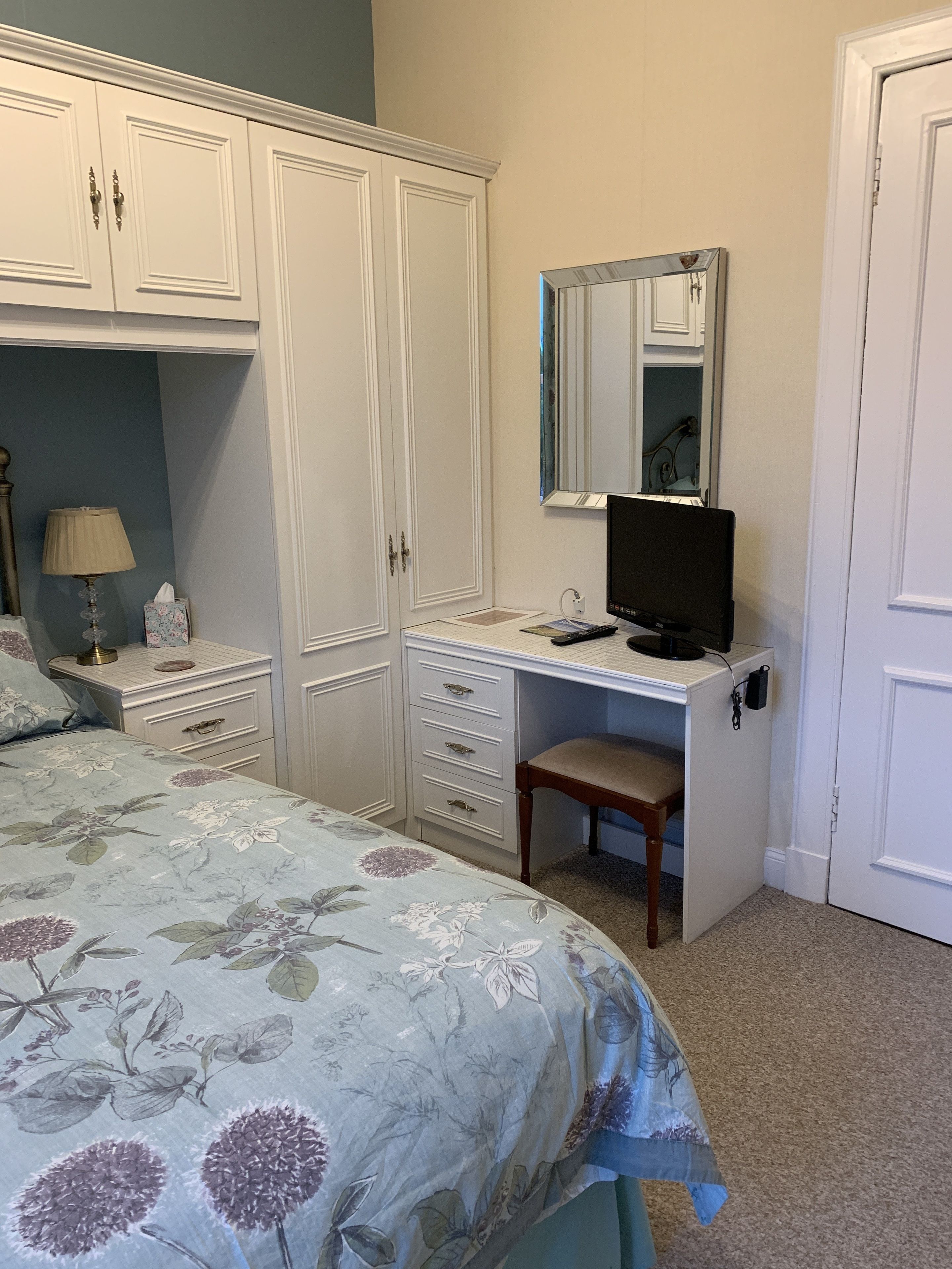 A bedroom with a bed, a desk, a chair, a wardrobe, and a mirror.