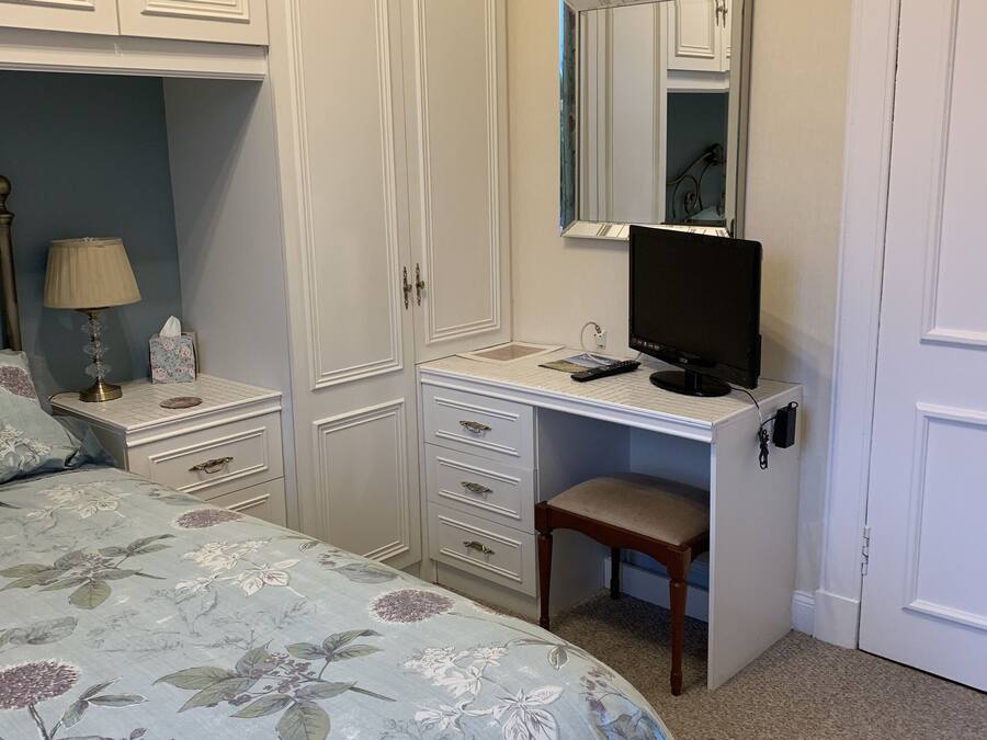 A bedroom with a bed, a desk, a chair, a wardrobe, and a mirror.