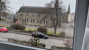 A view of a historic stone building with a prominent tower, a parking lot, and a road with cars. - Dunclutha Guest House (Leven)