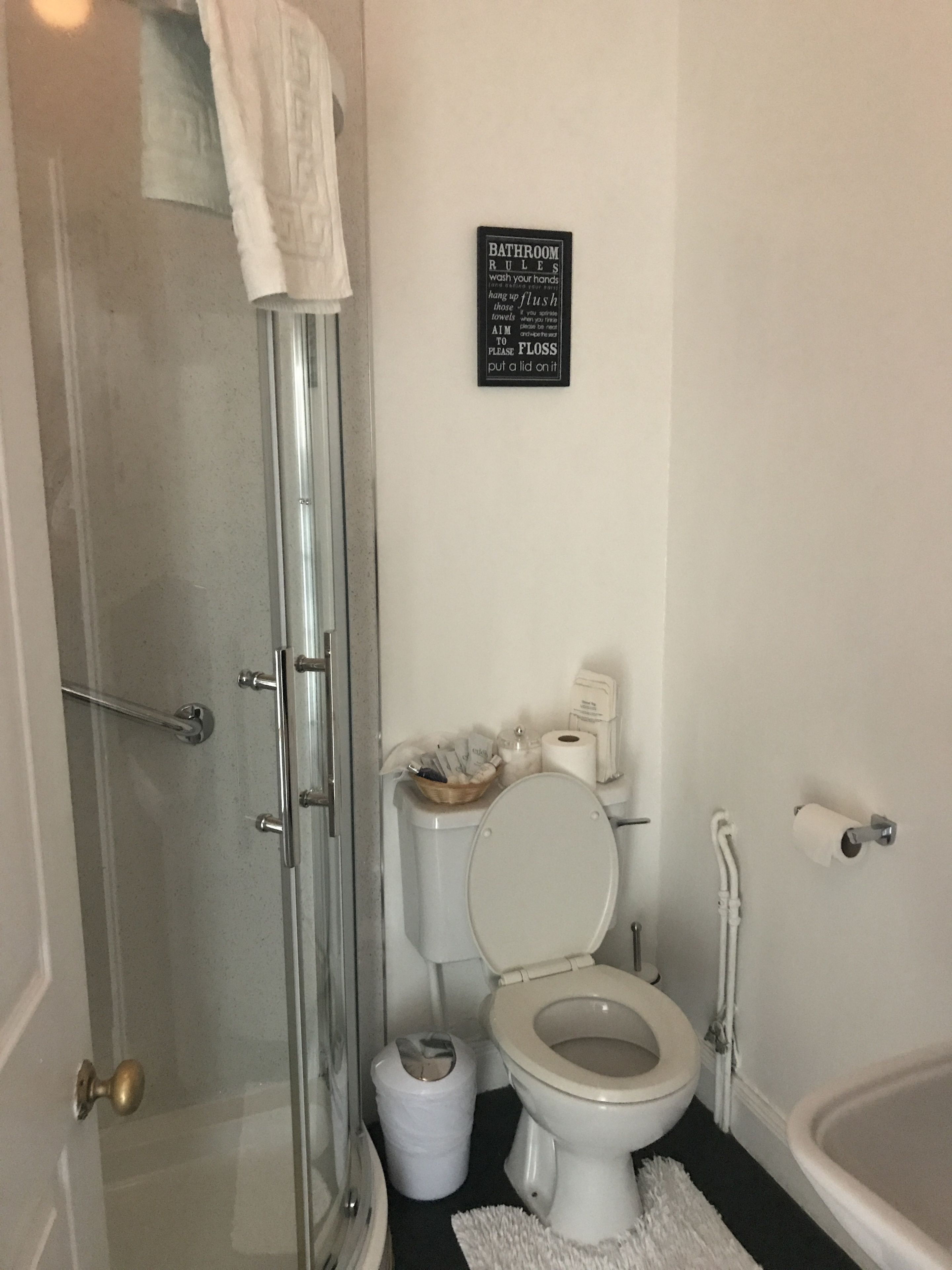 Un bagno con il water, una doccia e un cartello con le regole da rispettare.