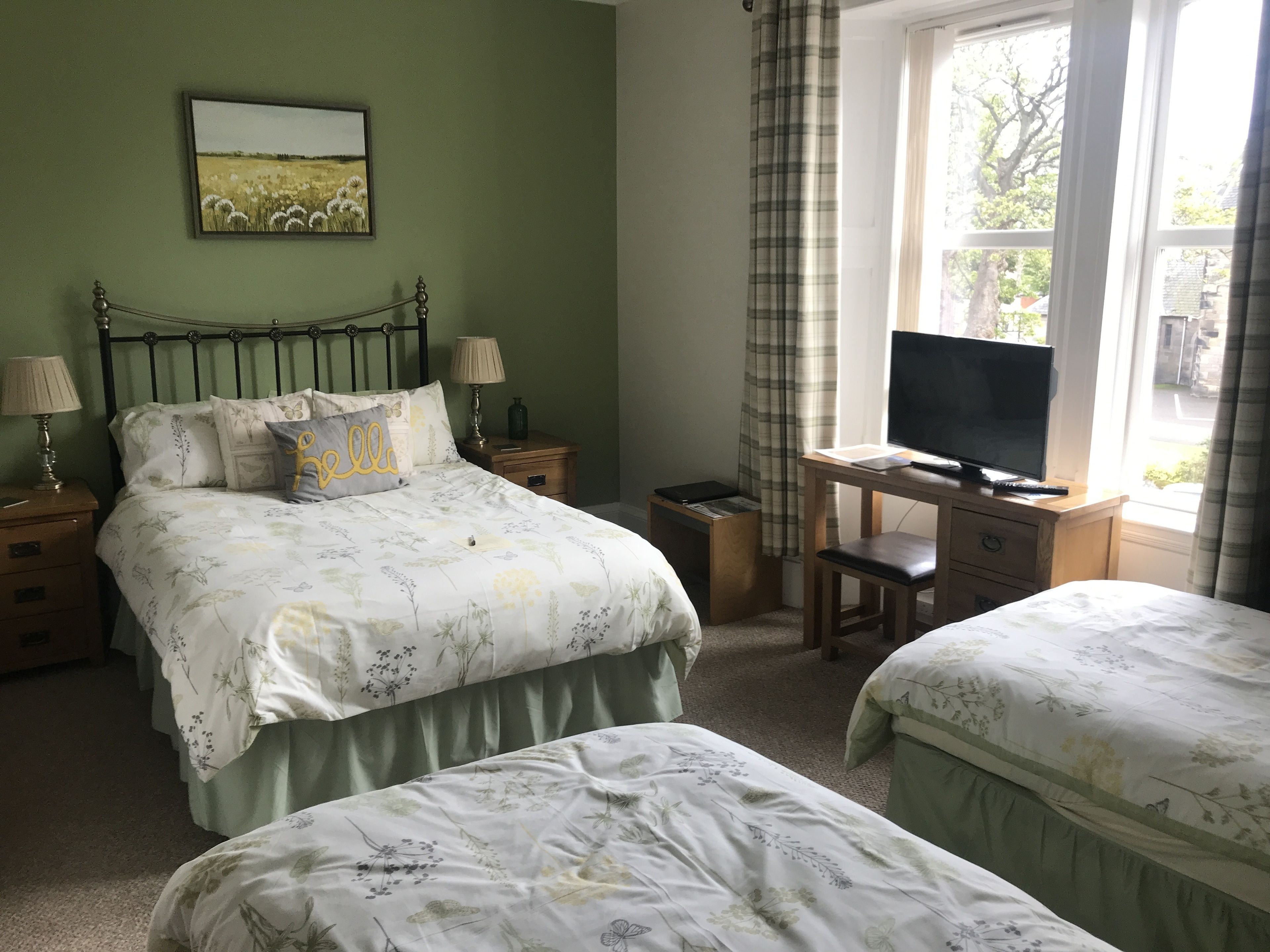 A bedroom with two beds, a desk with a TV, and a window with curtains.