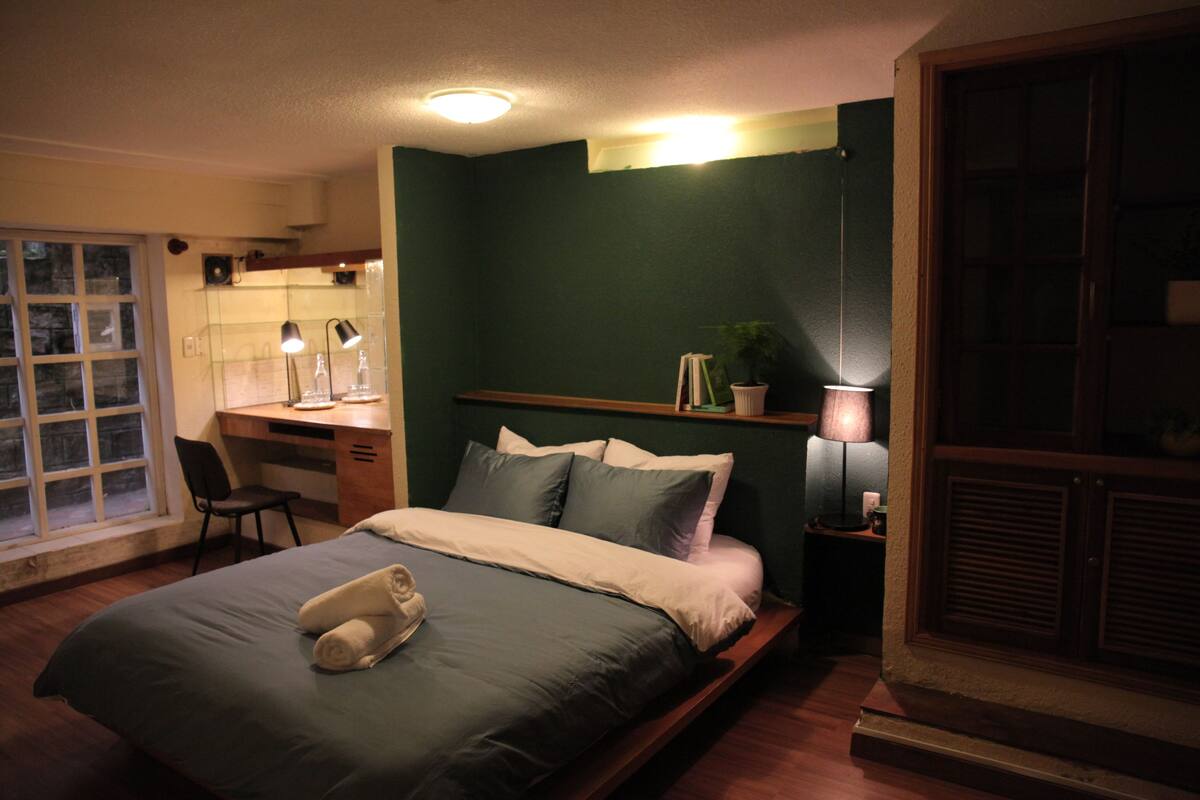 A bedroom with a bed, desk, chair, and a window.