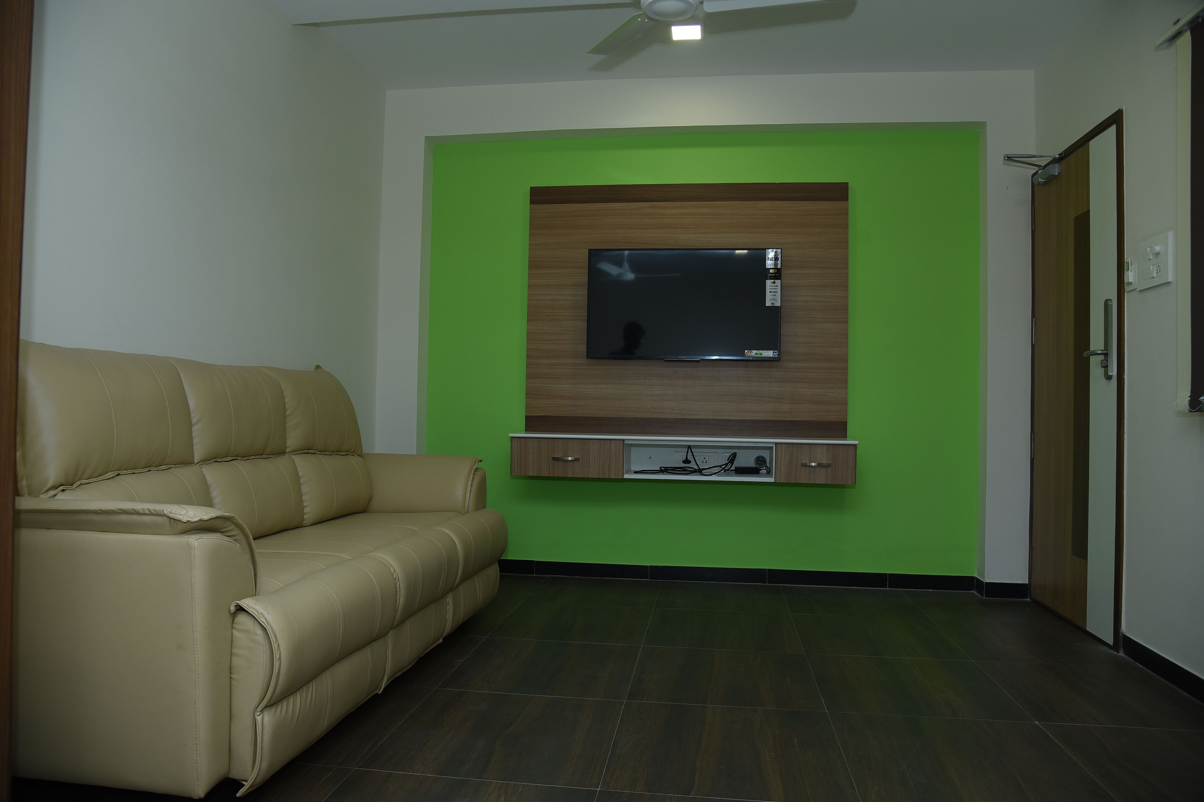 Una habitación con un sofá color beige, un televisor montado y una pared de acento verde.