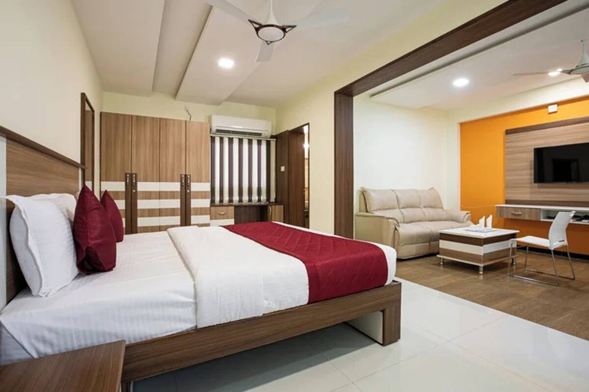 A modern bedroom with a bed, wardrobe, and a seating area with a sofa and a TV.