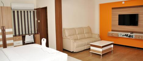 A modern hotel room with a bed, a sofa, a TV, and an air conditioning unit.