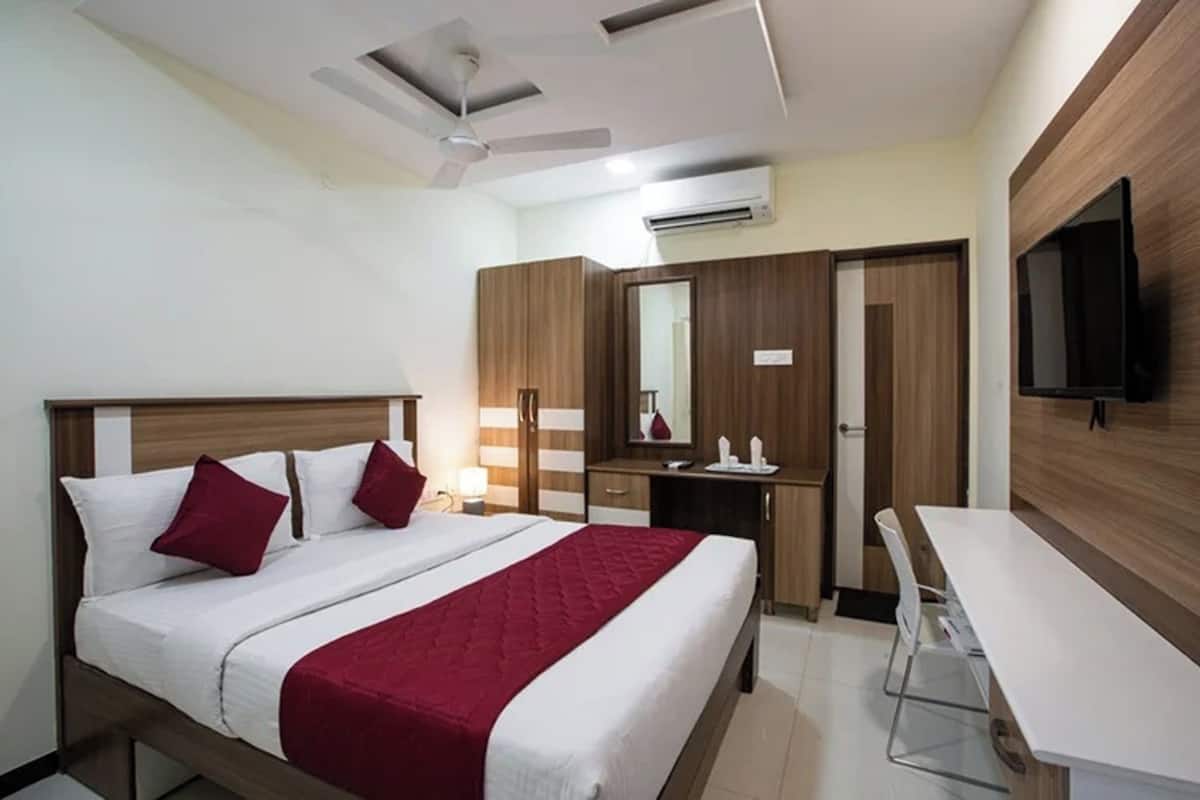 A hotel room with a bed, bedside table, desk, chair, TV, wardrobe, and ceiling fan.