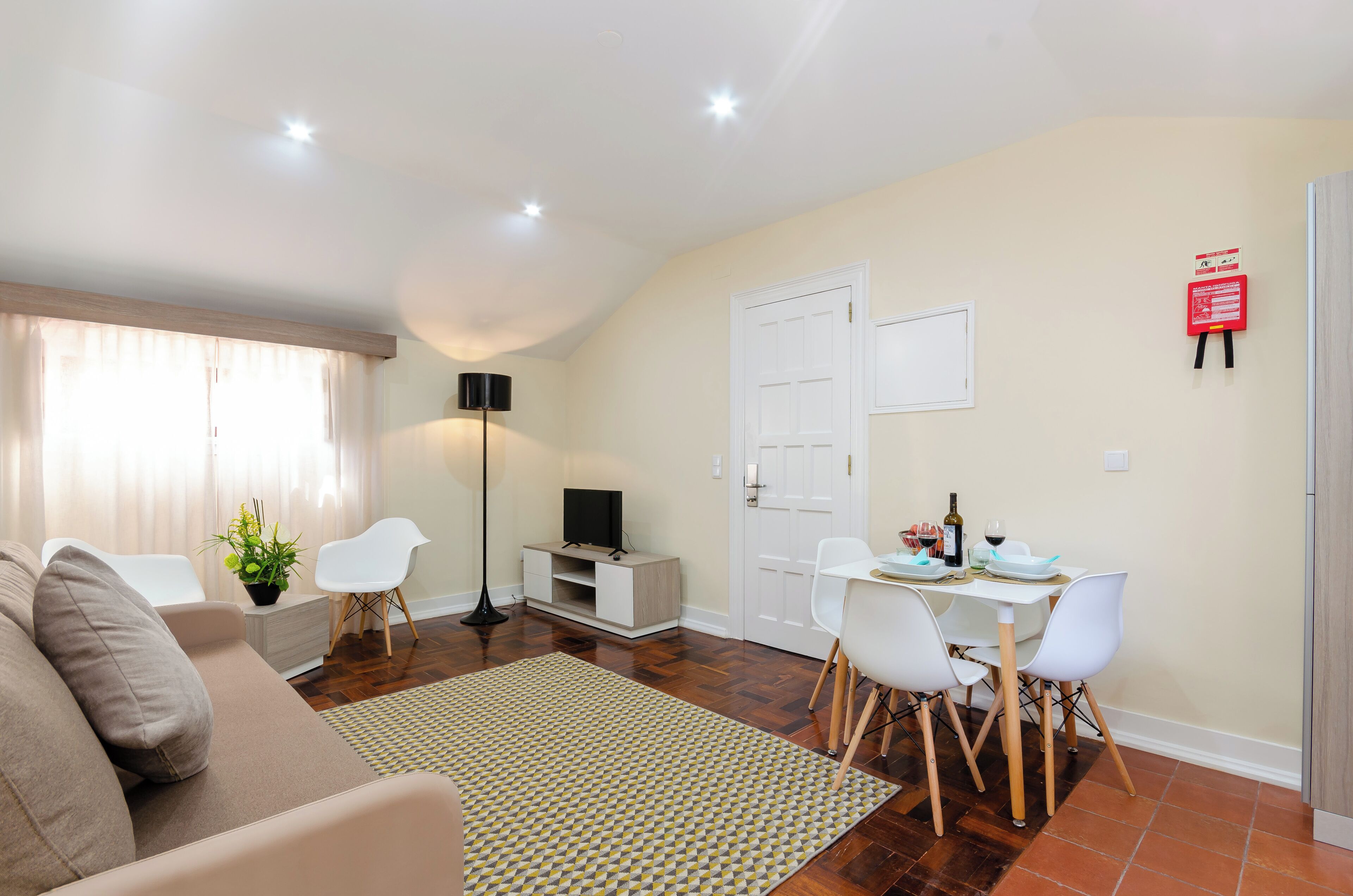 A living room with a sofa, a dining table with chairs, a TV stand, and a plant.