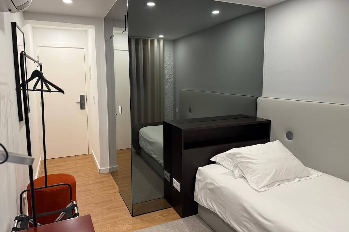 A modern hotel room with a bed, a desk, a chair, and a wardrobe.
