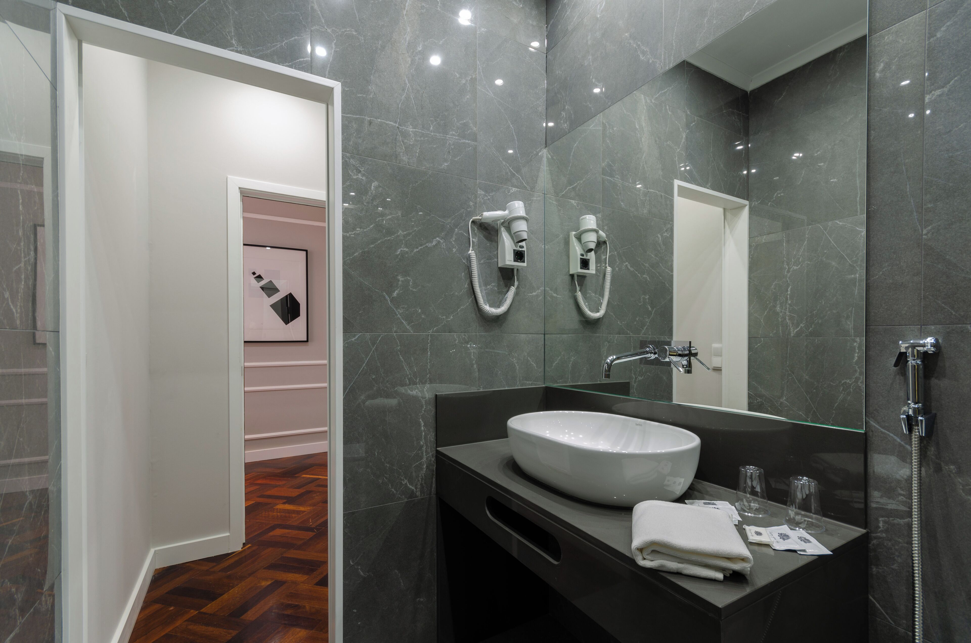 Un baño moderno con un espejo grande, un lavamanos blanco y una ducha.