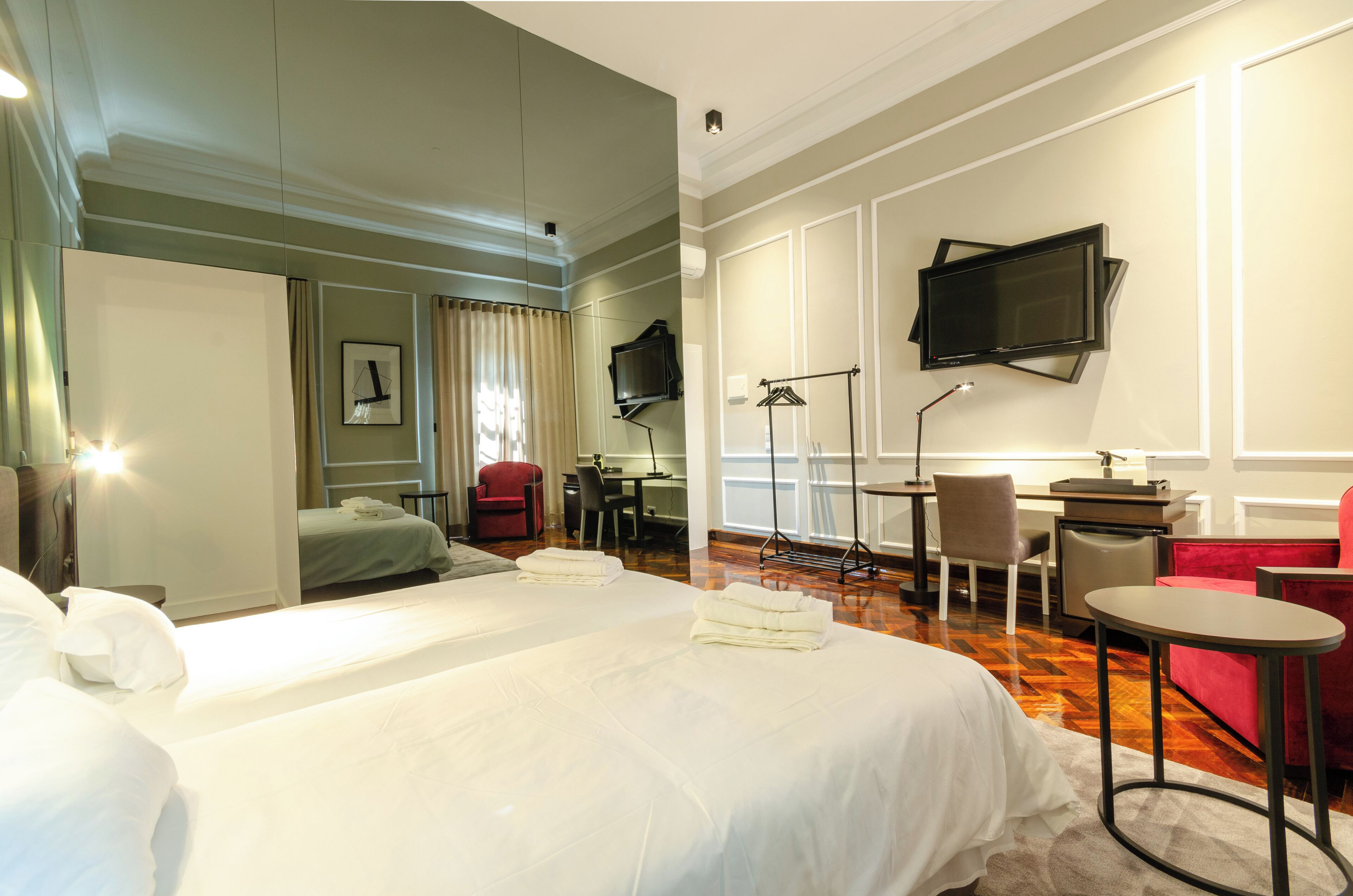 A hotel room with two beds, a desk, a chair, a TV, and a red sofa.