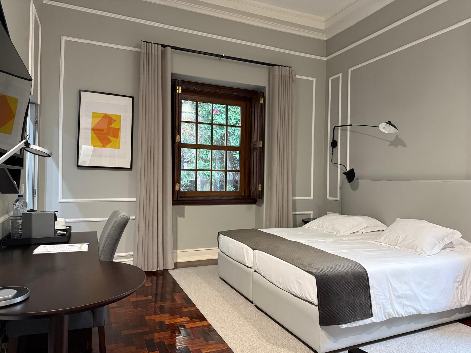 Ein Schlafzimmer mit Bett, Schreibtisch, Stuhl, einem Fenster mit Vorhängen und einer Wandlampe.