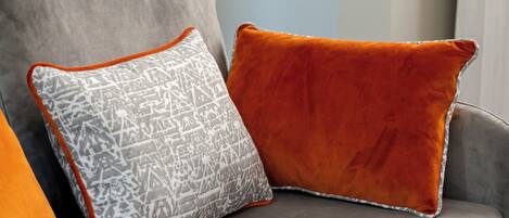 A grey sofa with two cushions, one patterned and one solid orange.